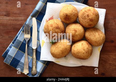 Mehrere frisch gebratene, traditionelle sizilianische Reisbällchen mit Füllung (arancini siciliani) werden von oben auf einem rustikalen Holztisch mit pla fotografiert Stockfoto