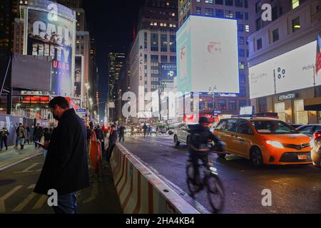 Die Nachtansicht der 7. Avenue in der Nähe von Madison Square Garden und Penn Station mit einem Mann, der auf sein Telefon schaut und einer Person auf dem Fahrrad dahinter.New York City.NY.USA Stockfoto