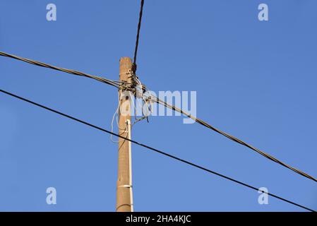 Die Spitze eines einfachen Strommostes, von dem aus verschiedene Stromkabel in verschiedene Richtungen verlaufen, gegen einen blauen Himmel Stockfoto