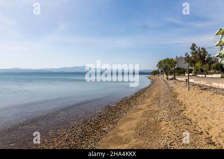 Ein Sandstrand irgendwo in griechenland. Einige rostige Pflöcke kommen aus dem Sand und genießen den Blick auf das Meer und die Berge im Hintergrund. Bäume sind auch auf dem Bild. Stockfoto