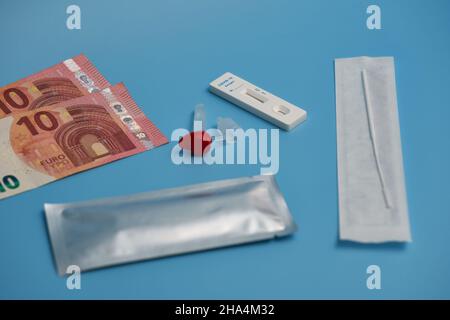 Antigen-Test auch Corona-Schnelltest mit Testkassette, Wattestäbchen und Probenröhrchen auf blauer Oberfläche. Geld. Seitenansicht. Stockfoto