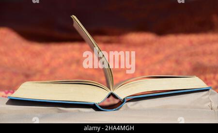 Ein offenes altes Buch liegt auf einer Liege in der Sonne und die Seiten des Buches werden vom Wind weggeblasen Stockfoto