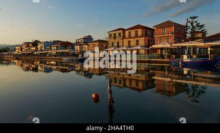 griechenland, griechische Inseln, ionische Inseln, lefkada oder lefkas, lefkada Stadt, Hauptstadt, Morgenlicht, Morgengrauen, Reihe von Häusern diagonal von der Seite, Weitwinkel-Ansicht, Häuser spiegeln sich im ruhigen Wasser des Kanals, rote Boje und Holzmast im Vordergrund Stockfoto