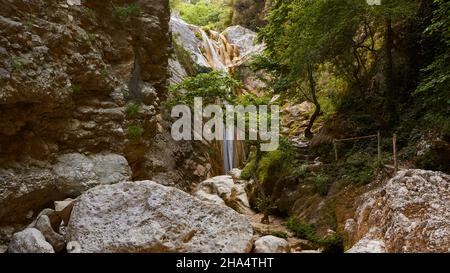 griechenland, griechische Inseln, ionische Inseln, lefkada oder lefkas, Bucht von nidri, Wasserfälle von nidri, Blick durch Felsen und Bäume zum Wasserfall, Felsbrocken im Vordergrund Stockfoto