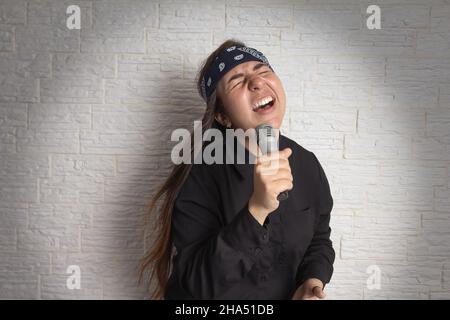 Trendy Mädchen mit ungewöhnlichen Frisur singen Karaoke mit Mikrofon auf der Bühne. Urlaub, Freizeit, Genuss, Musik, Sound, Leistungskonzept. Stockfoto