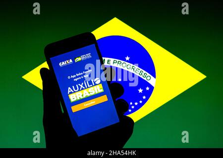 Barcelona, Katalonien, Spanien. 9th Dez 2021. In dieser Abbildung wird eine Auxilio Brasil App auf einem Smartphone mit einer brasilianischen Flagge im Hintergrund angezeigt. (Bild: © Thiago Prudencio/DAX via ZUMA Press Wire) Stockfoto