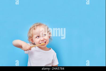 Das Kind putzt seine Zähne mit einer hölzernen Bambuszahnbürste auf blauem Hintergrund mit einem Kopierraum Stockfoto