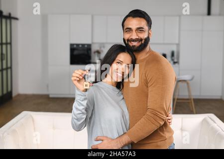 Glückliches indisches Familienpaar zeigt neue Hausschlüssel an die Kamera, während er im Haus posiert. Eigenheim, Immobilien und Wohnen. Hypotheken und Wohnungskauf Stockfoto