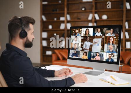 Virtuelle Konferenz mit Mitarbeitern. Junger Mann in formeller Kleidung, der PC für Videoanruf verwendet, mit Videobesprechung mit mehreren Personen zusammen. Remote-Work-Konzept Stockfoto