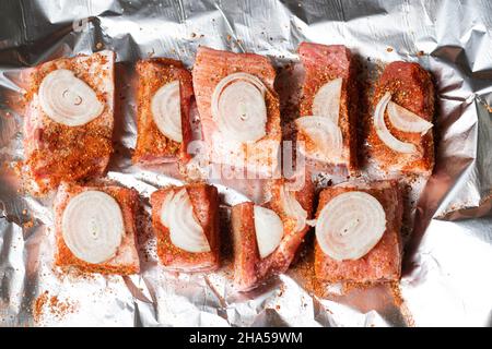 Rohe Schweineribs mit rohen Zwiebeln liegen auf Folie, fertig zum Backen im Ofen. Stockfoto