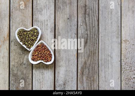 Sichuan rot und grün Pfefferkorn Nahaufnahme in herzförmiger Platte auf Holzbrett Hintergrund Stockfoto