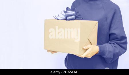 Eine junge Frau in EINEM SEHR PERI Sweatshirt hält eine Pappschachtel mit einer SEHR PERI Schleife. Online-Shopping Sale. Geschenke in den Händen der Frau. Express-Lieferung. Stockfoto