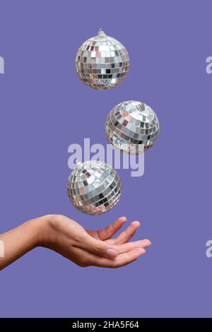 Disco Ball schwimmt in der Luft unter der Hand vor hellviolettem Hintergrund Stockfoto