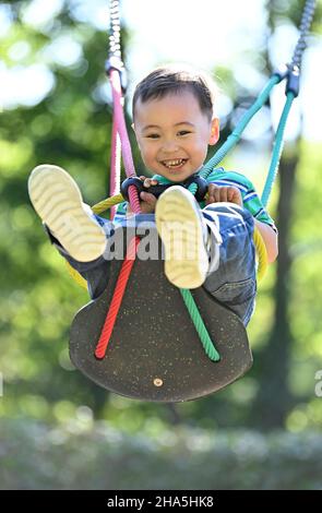 Kleinkind, 2 Jahre, multiethnisch, eurasisch, lacht, schaukelt auf einer Kinderschaukel, blaubeuren, baden-württemberg, deutschland Stockfoto