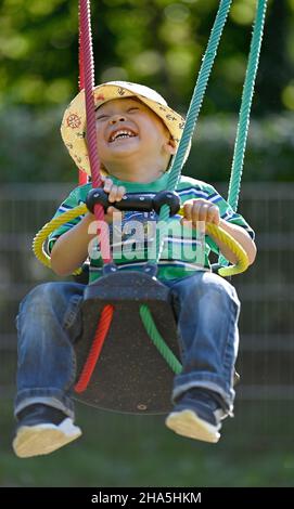 Kleinkind, 2 Jahre, multiethnisch, eurasisch, lacht, schaukelt auf einer Kinderschaukel, blaubeuren, baden-württemberg, deutschland Stockfoto