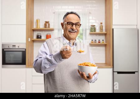 Lächelnder reifer Mann, der in einer Küche steht und Cornflakes isst Stockfoto