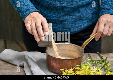 Arbeitsschritte mit Fenchel und Fenchelsamen für die Herstellung von Fenchelsaft füllt die Frau Rohrzucker in einen Kupfertopan Stockfoto