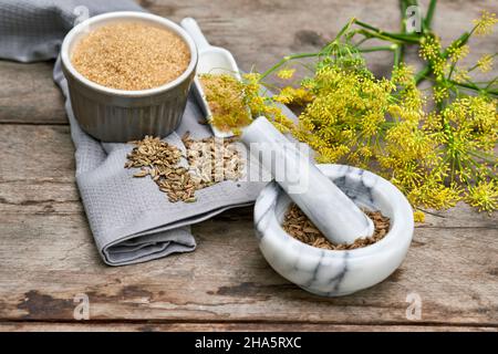 Arbeitsschritte mit Fenchel- und Fenchelsamen zur Herstellung von Fenchelsaft, den Zutaten Rohrzucker, Fenchelsamen im Mörser und Fenchelsamen auf einem Holztisch Stockfoto