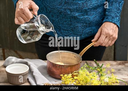 Arbeitsschritte mit Fenchel und Fenchelsamen für die Zubereitung von Fenchelsaft füllt die Frau Wasser aus einem Glaskrug in einen Kupferauflauf mit Rohrzucker Stockfoto