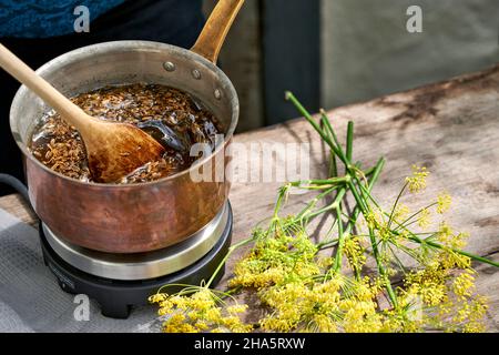 Arbeitsschritte mit Fenchelsamen und Fenchelsamen zur Herstellung von Fenchelsaft, mit einem Holzlöffel werden die Fenchelsamen zu einer Rohrzuckerlösung gerührt und erhitzt Stockfoto