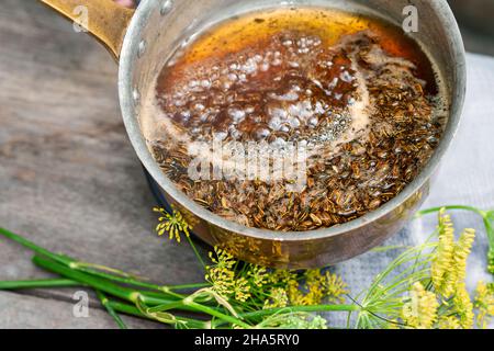 Arbeitsschritte mit Fenchel- und Fenchelsamen für die Zubereitung von Fenchelsaft, Blick in einen Kupfertopan mit einer kochenden Lösung aus Fenchelsamen und Rohrzucker, daneben Fenchelsamen auf einem Holztisch Stockfoto