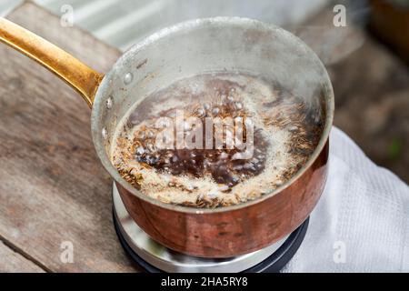 Arbeitsschritte mit Fenchel- und Fenchelsamen zur Herstellung von Fenchelsaft, Blick in einen Kupfertopf mit einer kochenden Lösung aus Fenchelsamen und Rohrzucker Stockfoto