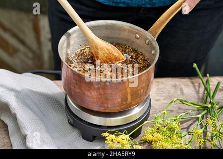 Arbeitsschritte mit Fenchelsamen und Fenchelsamen zur Herstellung von Fenchelsaft, mit einem Holzlöffel werden die Fenchelsamen zu einer Rohrzuckerlösung gerührt und erhitzt Stockfoto