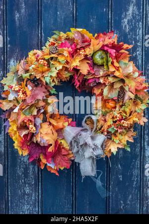 Farbenfroher Kranz aus Herbstblättern und Blumen an einer Landhaustür, runder Blumenkranz voller Herbstfarben an einer alten hölzernen Landhaustür. Stockfoto