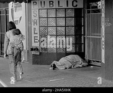 Eine Frau, die ein Kind auf dem Rücken trägt, kommt am 1980s auf einem Bürgersteig in San Francisco an einer Person vorbei, die in einer Tür schläft Stockfoto
