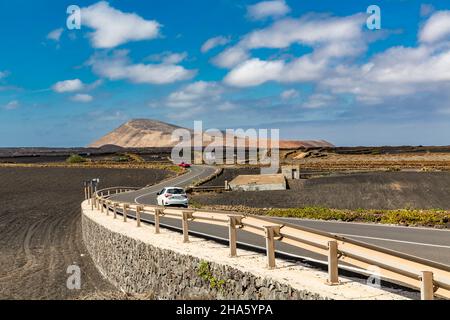 Straße in der Nähe von mancha blanca, tinajo, hinter den Vulkanen montana Caldera blanca, 458 m, und montana Caldereta, Nationalpark Los volcanes, parque Natural de los volcanes, Naturschutzgebiet, lanzarote, Kanaren, kanarische Inseln, spanien, europa Stockfoto