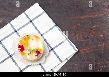 Kuchen mit Gelee, Kiwi, Kirschen und Mango auf dem Tisch. Leckeres Mini-Dessert auf einem hölzernen Hintergrund, Nahaufnahme. Stockfoto