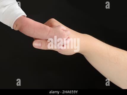 Nahaufnahme der Hand einer erwachsenen Person, die die Hand eines Babys berührt. Hände isoliert auf schwarzem Hintergrund. Stockfoto