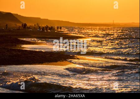 Nahaufnahme der Flutwassersurfen auf dem sandigen Ufer unter der goldenen Sonne mit entkofften Menschen im Hintergrund. Selektiver Fokus Stockfoto