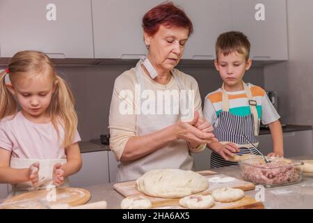 Oma zeigt den Zwillingen, wie man ein traditionelles Fleischgericht zubereitet Stockfoto