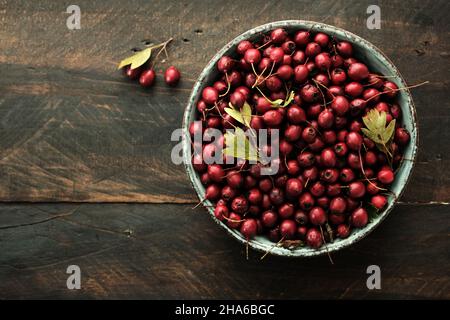 Eine Schale mit roten Beeren aus Weißdorn (Crataegus monogyna) auf dunklem rustikalem Holztischhintergrund Stockfoto