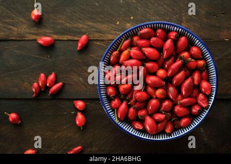 Eine Schüssel mit Hundsrosen (Rosa Canina) rote Hüften auf einem rustikalen Holztisch, Draufsicht Stockfoto