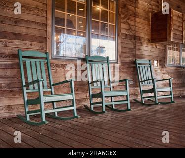 Drei grüne Schaukelstühle auf einer großen Holzterrasse im ländlichen Alabama, USA. Stockfoto