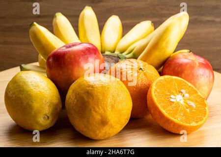 Verschiedene reife tropische Früchte auf Holzbrett. Verschiedene reife süße Früchte, Bananenbündel, eineinhalb Orangen, rote Äpfel und reifer Lemmon. Stockfoto