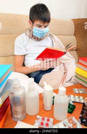 Kranker Teenager in Grippe-Maske mit den Büchern auf dem Sofa Stockfoto