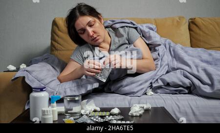 Kranke Frau nimmt Medikamente und trinkt Wasser auf dem Sofa Stockfoto