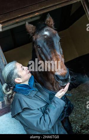 Eine reife Reiterin verbringt die letzten kostbaren Stunden, bevor ein Pferd aufgrund von schlechtem Gesundheitszustand und Alter abgesetzt wird. Stockfoto