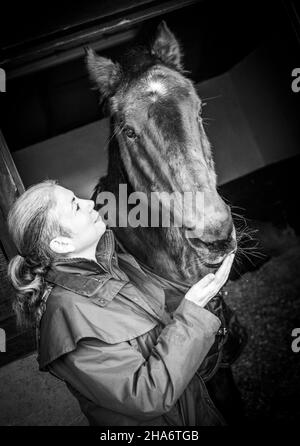 Eine reife Reiterin verbringt die letzten kostbaren Stunden, bevor ein Pferd aufgrund von schlechtem Gesundheitszustand und Alter abgesetzt wird. Stockfoto