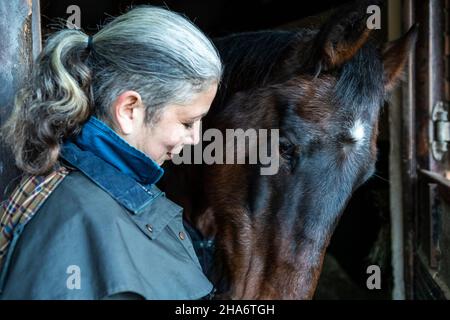 Eine reife Reiterin verbringt die letzten kostbaren Stunden, bevor ein Pferd aufgrund von schlechtem Gesundheitszustand und Alter abgesetzt wird. Stockfoto
