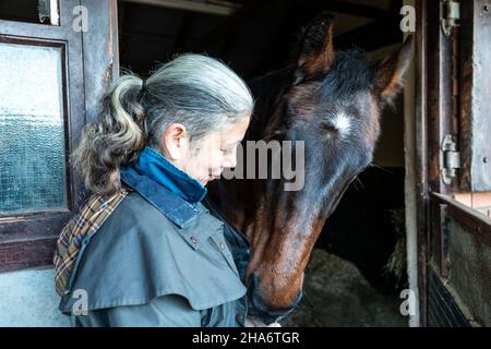 Eine reife Reiterin verbringt die letzten kostbaren Stunden, bevor ein Pferd aufgrund von schlechtem Gesundheitszustand und Alter abgesetzt wird. Stockfoto