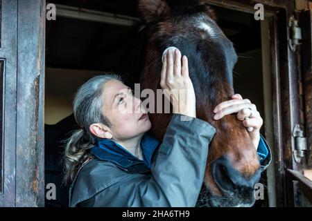 Eine reife Reiterin verbringt die letzten kostbaren Stunden, bevor ein Pferd aufgrund von schlechtem Gesundheitszustand und Alter abgesetzt wird. Stockfoto