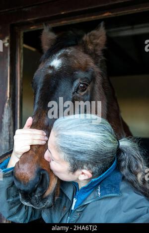 Eine reife Reiterin verbringt die letzten kostbaren Stunden, bevor ein Pferd aufgrund von schlechtem Gesundheitszustand und Alter abgesetzt wird. Stockfoto