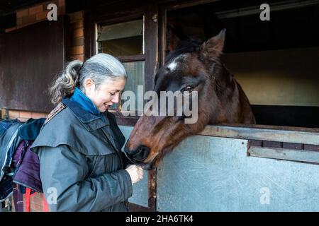 Eine reife Reiterin verbringt die letzten kostbaren Stunden, bevor ein Pferd aufgrund von schlechtem Gesundheitszustand und Alter abgesetzt wird. Stockfoto
