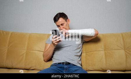 Brunet Mann pickt Nase mit gebrochenem Arm scrollende Social Media Stockfoto