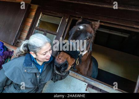 Eine reife Reiterin verbringt die letzten kostbaren Stunden, bevor ein Pferd aufgrund von schlechtem Gesundheitszustand und Alter abgesetzt wird. Stockfoto