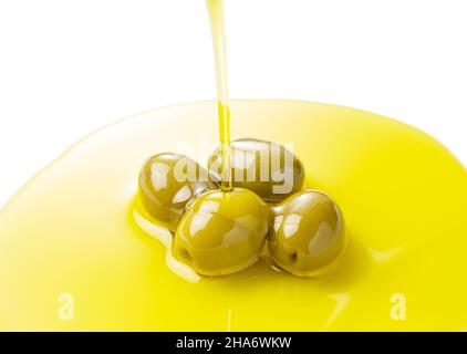 Der Moment, in dem Olivenöl über Oliven gegossen wird, die auf weißem Hintergrund stehen Stockfoto